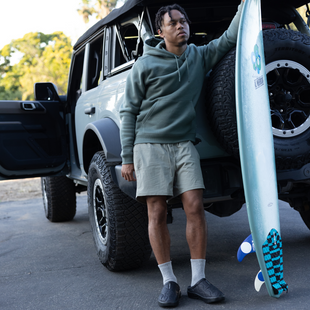 model next to car holding surf board wearing oocoozie mule thermo black