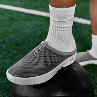 close up of model wearing MEN'S OOCOOZIE SPORT MULE - SLATE in field with foot on sports ball