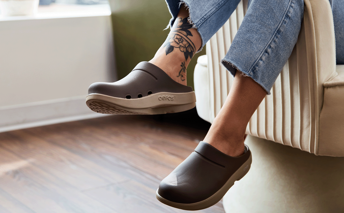 Person wearing brown clogs with tattoos on a chair