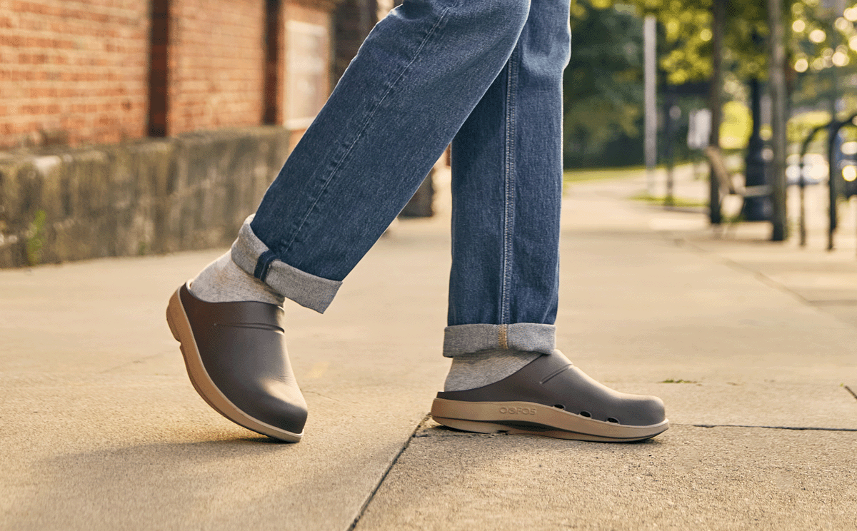 Person wearing brown shoes and blue jeans on a sidewalk.