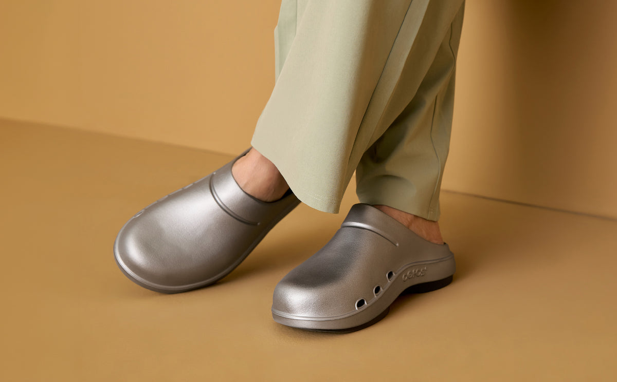 model standing in studio with orange background wearing silver clogs | lifestyle
