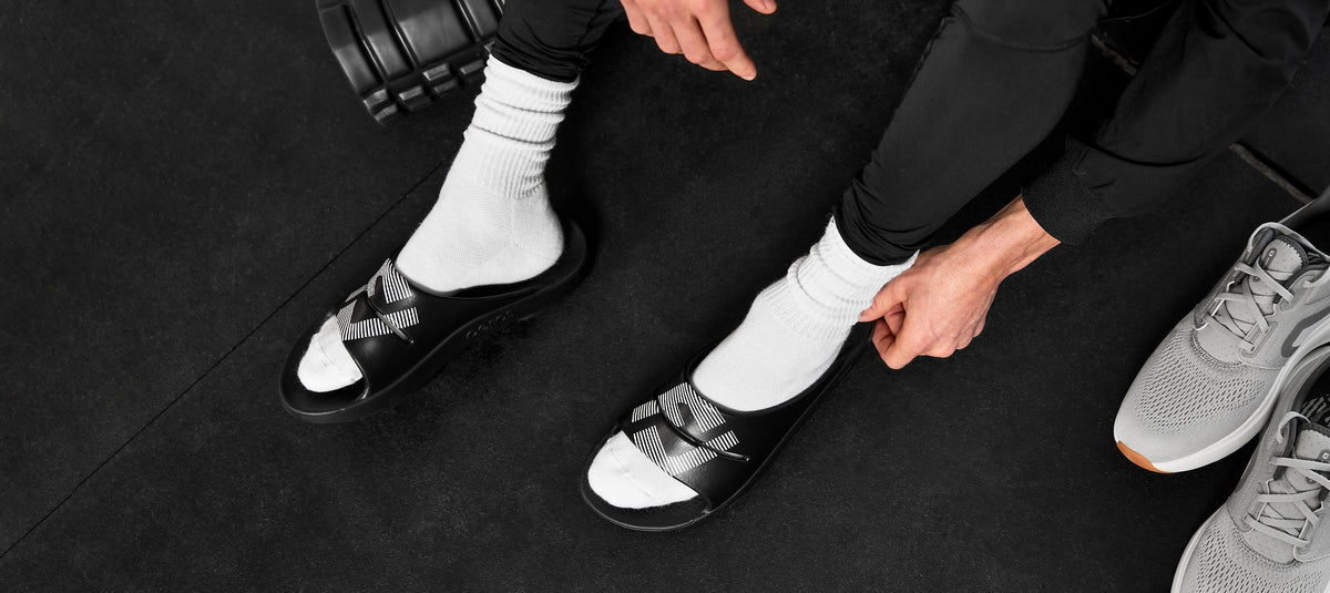 top view of model in gym wearing footjoy x oofos ooahh sport slide black