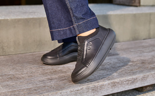 Person wearing black slip-on shoes and blue jeans sitting on a wooden bench | lifestyle