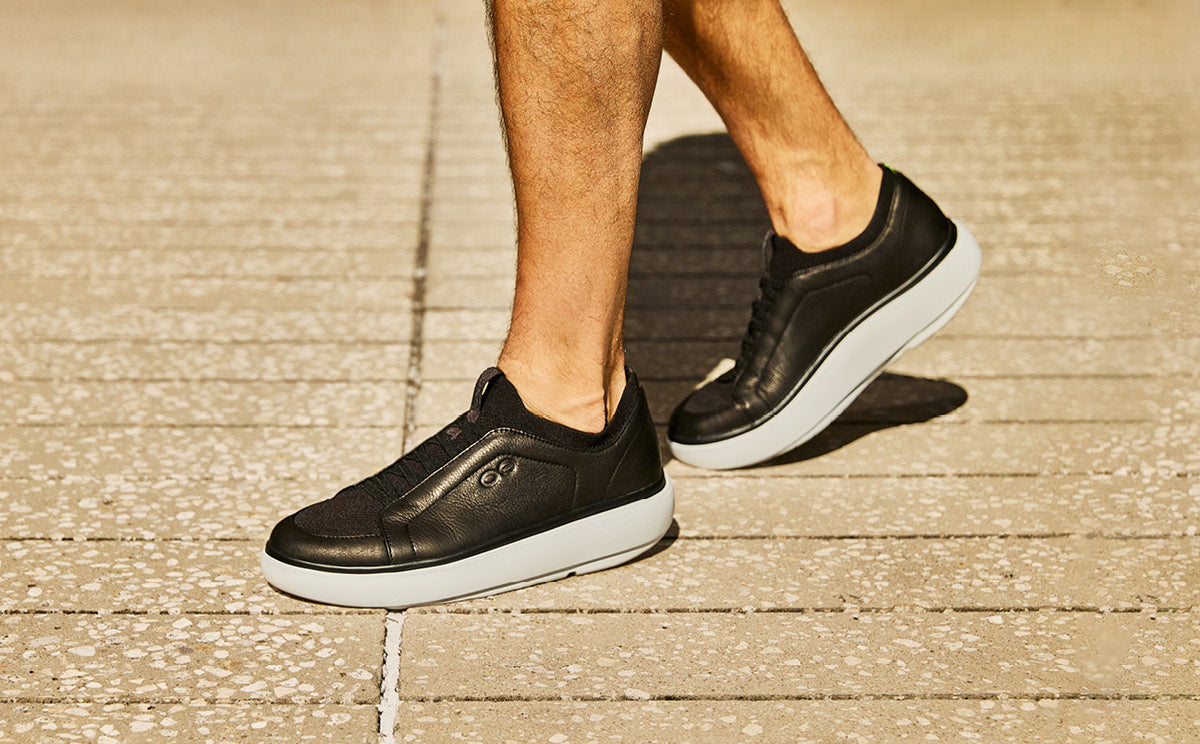 Black sneakers with white soles worn by a person on a textured surface| lifestyle