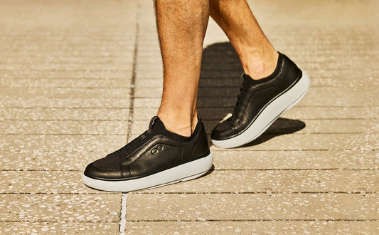 Black sneakers with white soles worn by a person on a textured surface| lifestyle
