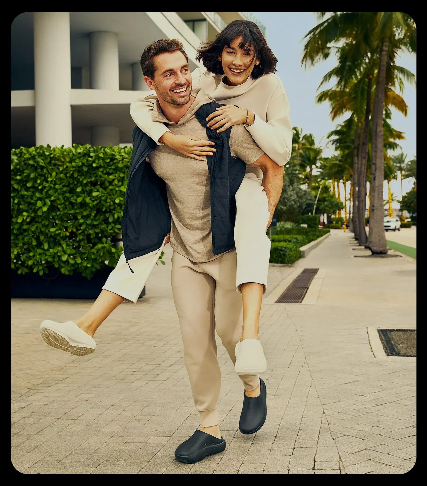Man carrying a woman on a sidewalk with palm trees in the background