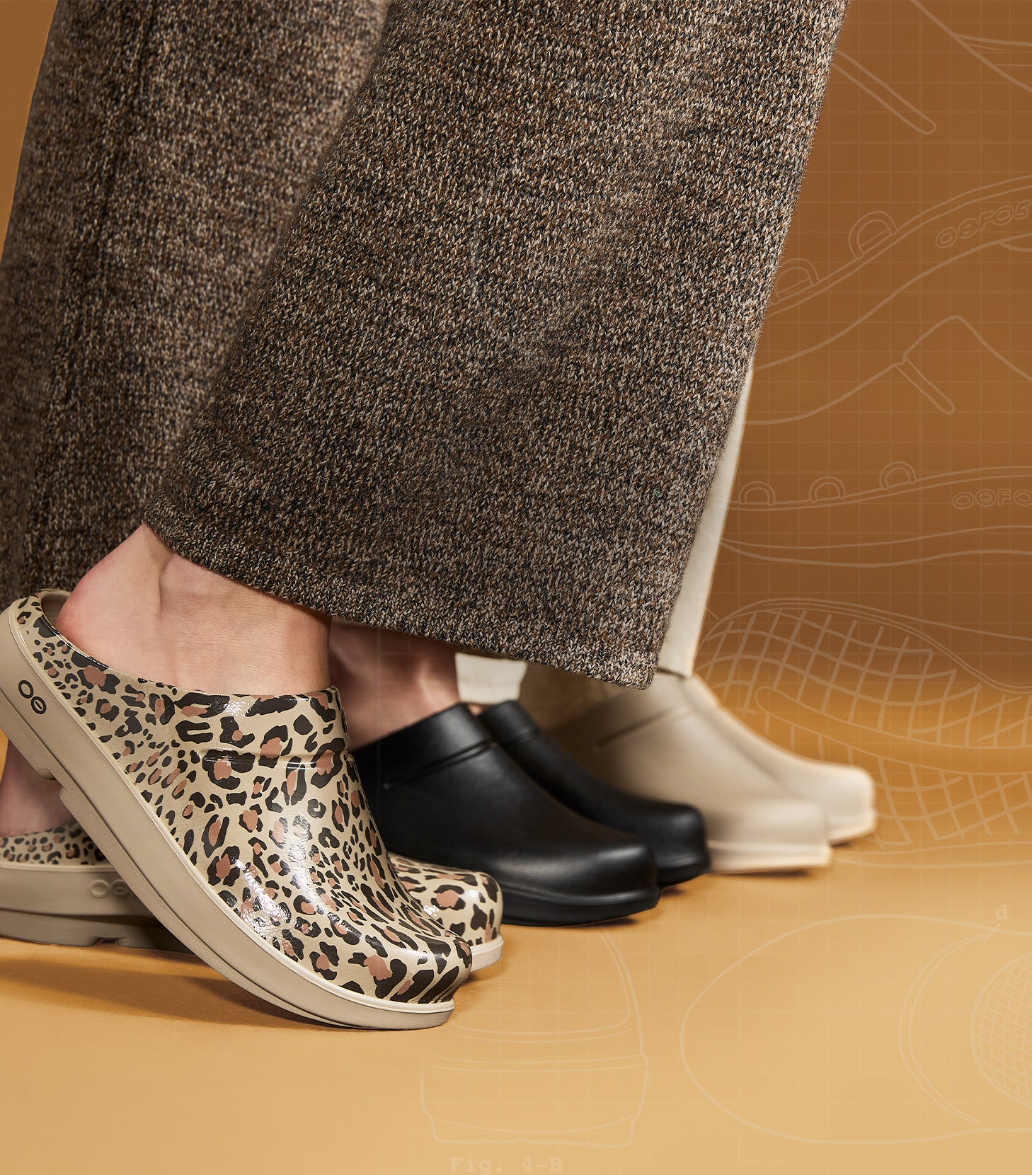 Leopard print clog shoe in the foreground, with black and off-white clogs lined up behind it on a warm tan studio background. A person's lower legs and feet are visible wearing the shoes.
