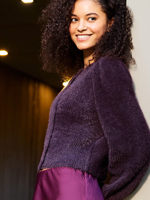 Woman wearing a purple knitted cardigan against a blurred indoor background