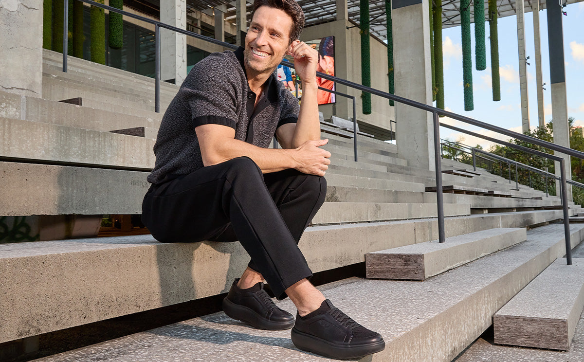 Man sitting on steps outdoors with a modern building in the background | lifestyle
