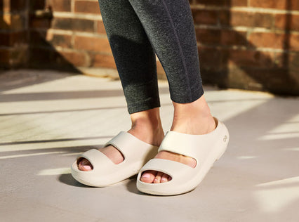 Person wearing chalk sandals on a concrete surface with a brick wall in the background