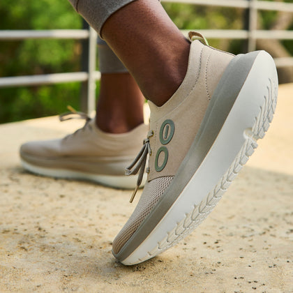 Beige casual shoes with white soles worn outdoors on a concrete surface.