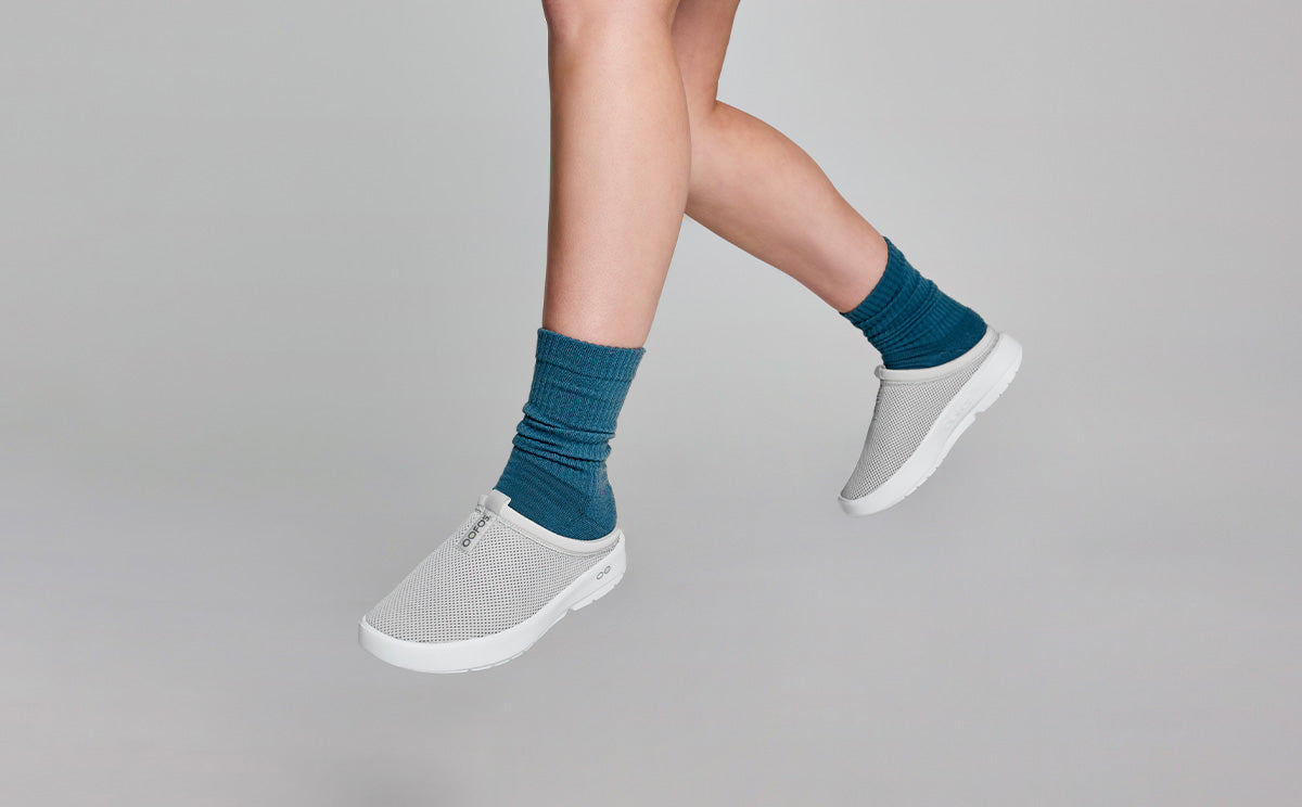 Women's OOcoozie Sport Mule - Gray model hanging in studio with feet dangling | lifestyle