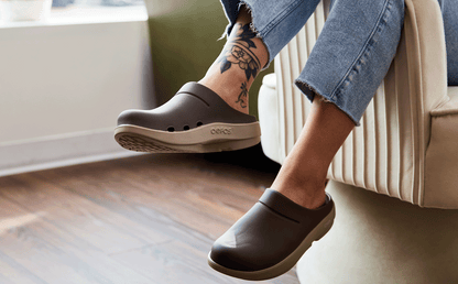 Person wearing brown clogs with tattoos on a chair