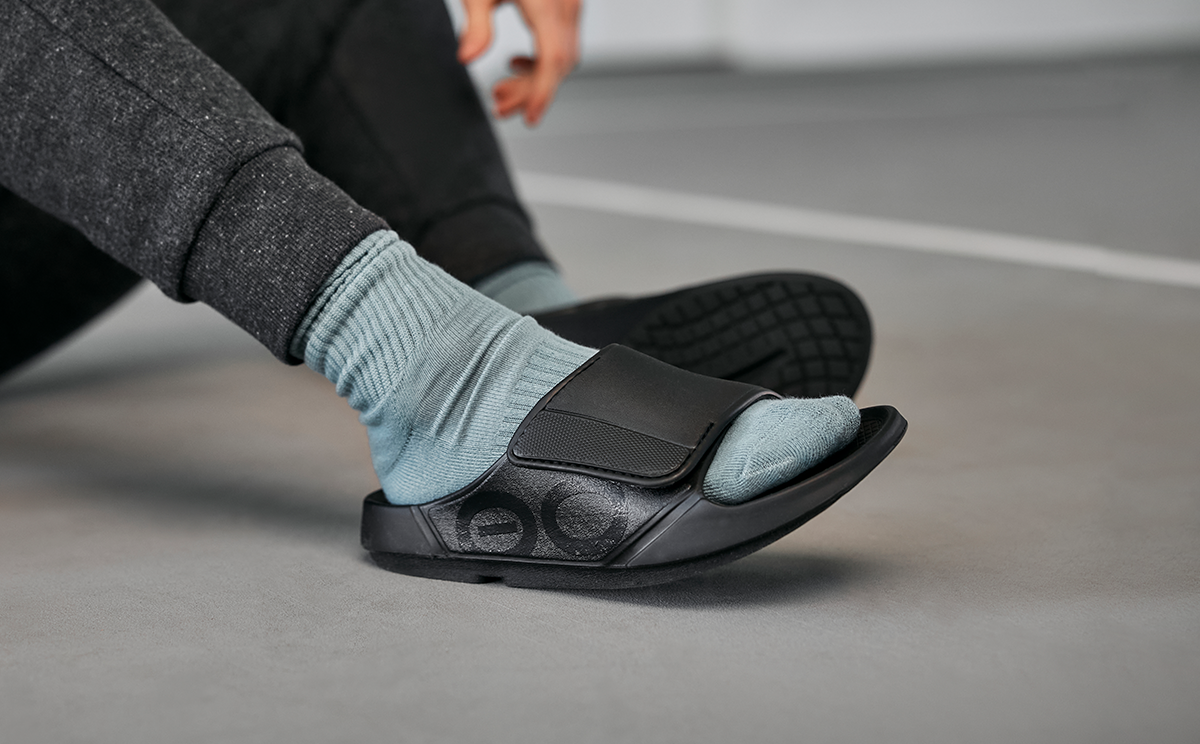 Men's OOahh Sport Flex Sandal - Matte Black close up of shoes on model sitting in gym | lifestyle