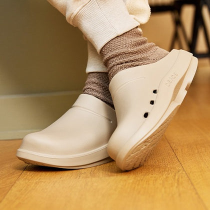 Nomad clog worn with brown socks on a wooden floor.