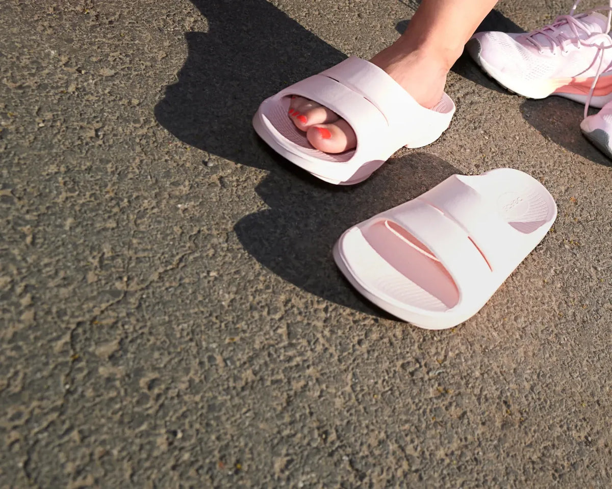 Pink OOFOS recovery slides on a running track