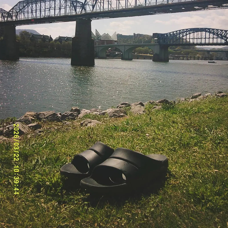 Black OOFOS slides by a river