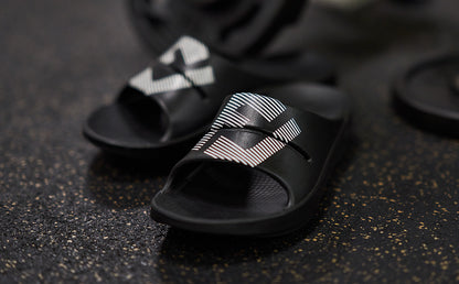 FJ X OOFOS Men's OOahh Sport Slide Sandal - Black close up of shoes on gym floor | lifestyle