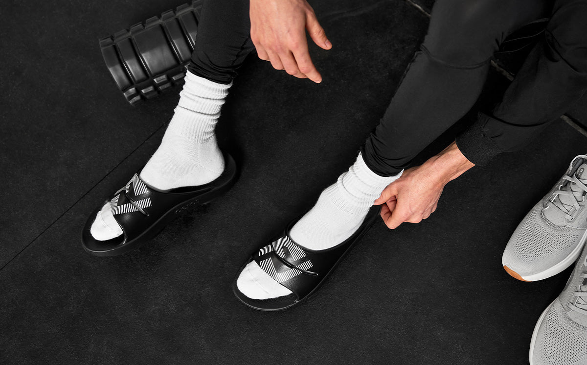 FJ X OOFOS Men's OOahh Sport Slide Sandal - Black top view of shoes on model in gym | lifestyle