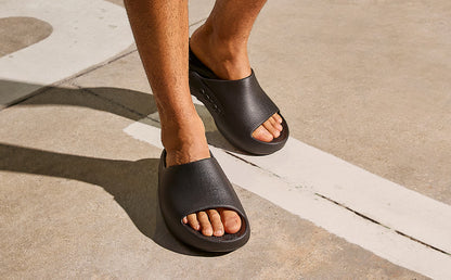 Person wearing black sandals on a concrete surface | lifestyle
