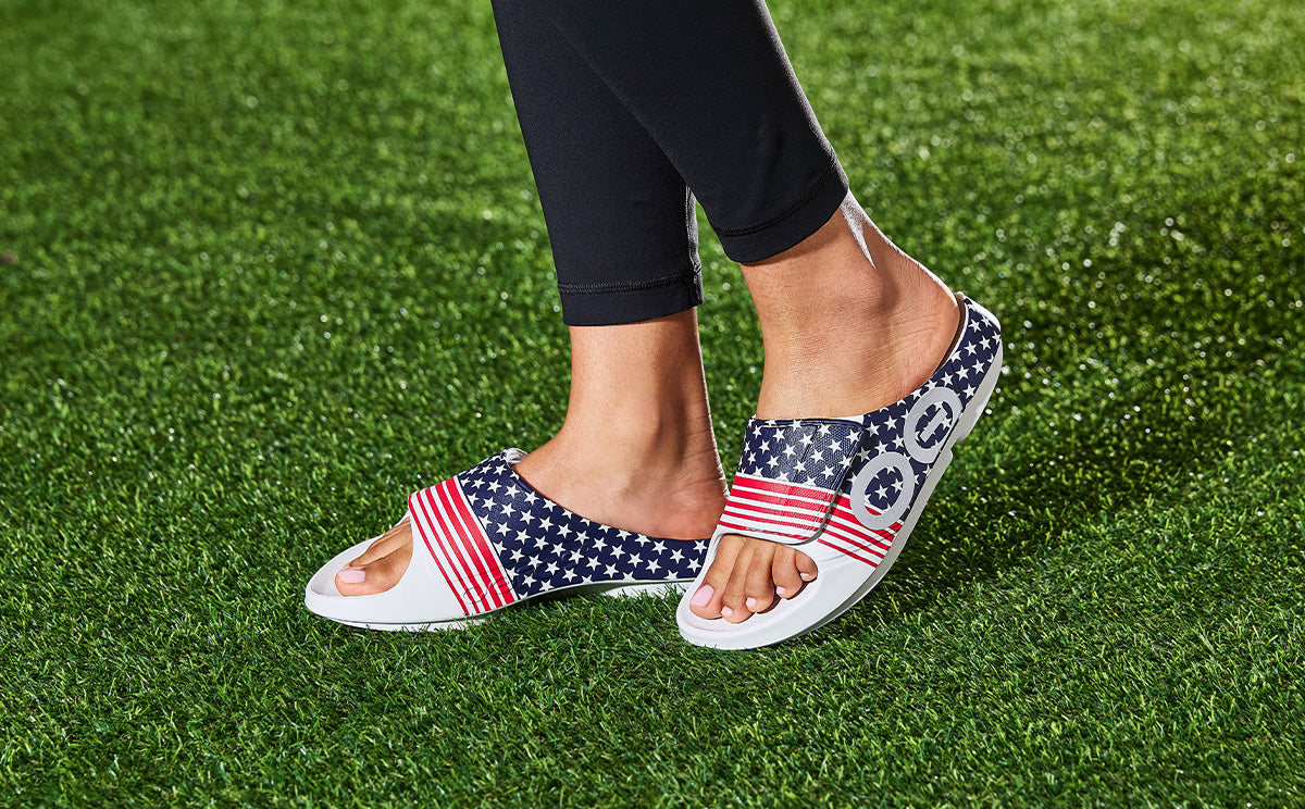 red white and blue oofos sport flex on grass field | lifestyle