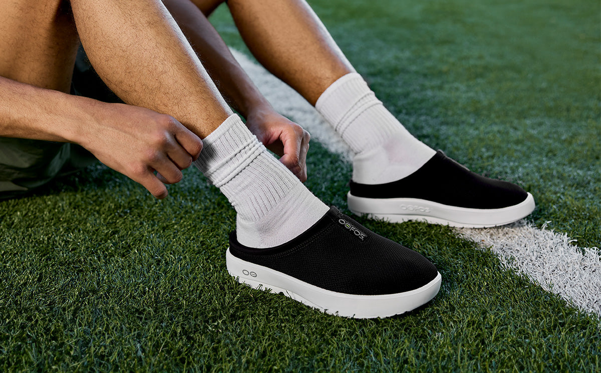Men's OOcoozie Sport Mule - White Black male model sitting on field | lifestyle