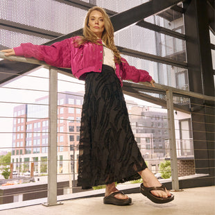 Woman in pink jacket and black skirt standing on a modern staircase with cityscape background