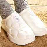 White quilted slippers with a visible brand logo on a wooden floor.