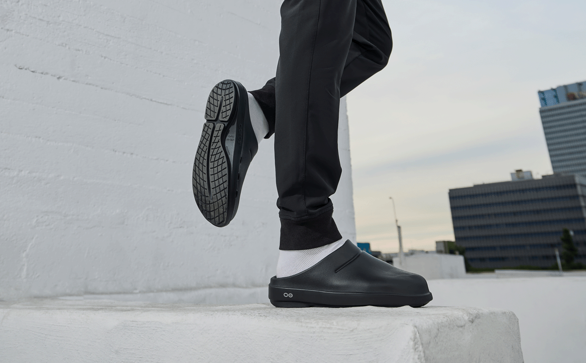 Men's OOcloog Clog - Black model standing on one foot on block outside | lifestyle