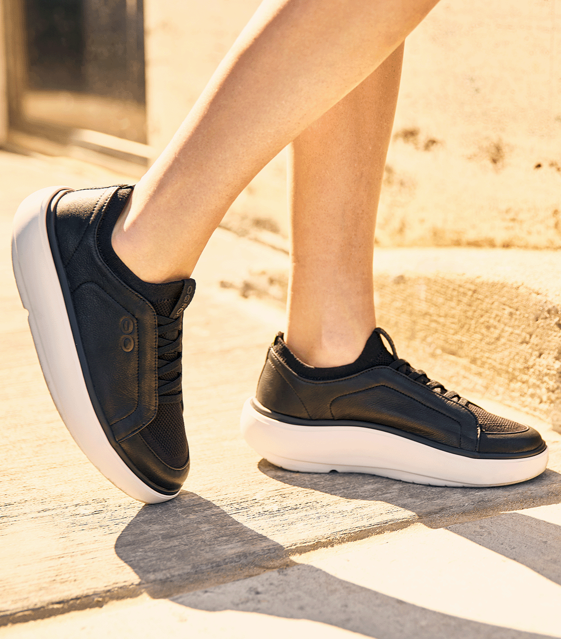 Black sneakers with white soles worn on concrete outside