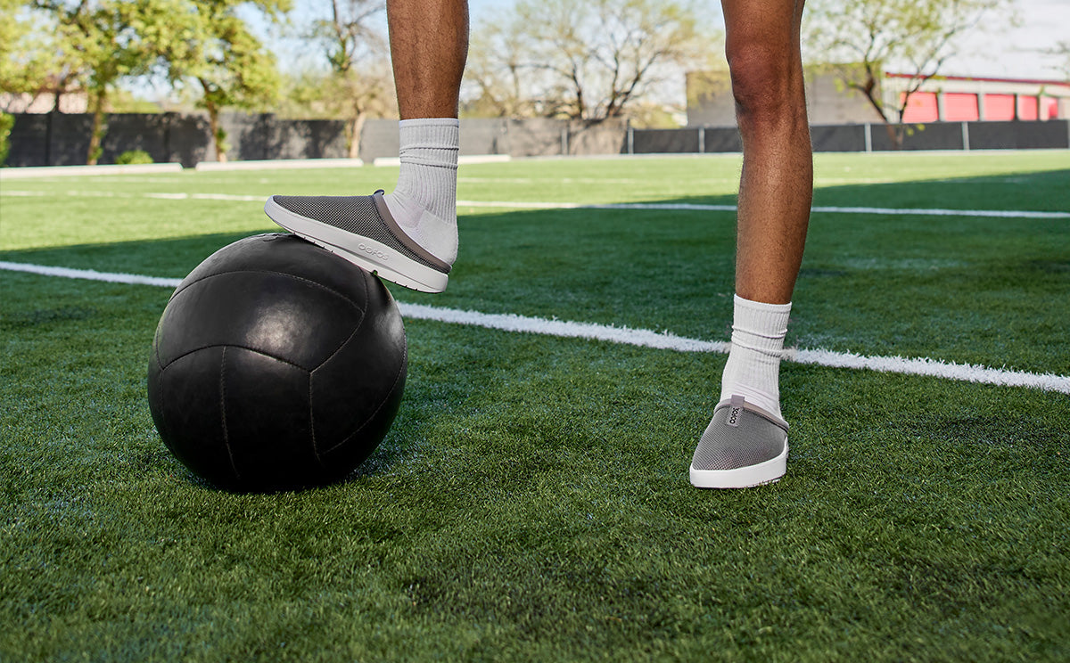 Men's OOcoozie Sport Mule - Slate front view of model in field with foot on sports ball | lifestyle