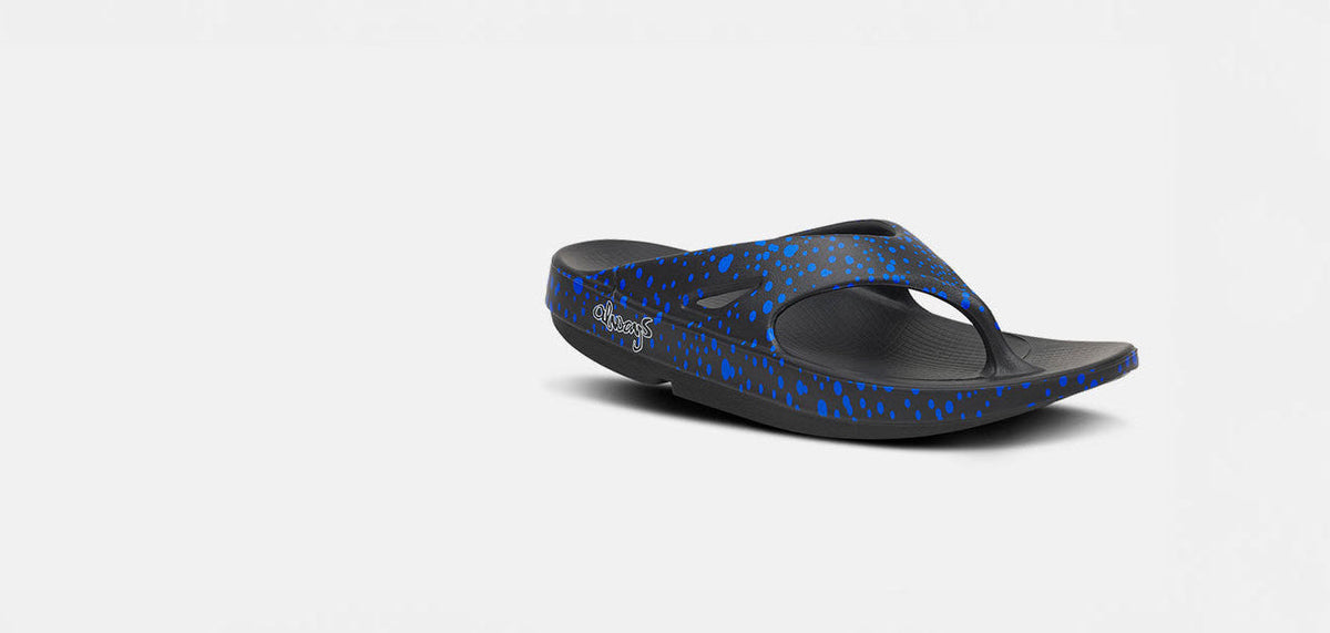 A single black flip-flop sandal with a blue speckled pattern, shown from a side profile on a light gray background.