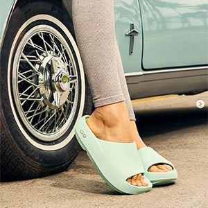 Person wearing light blue sandals next to a classic car wheel